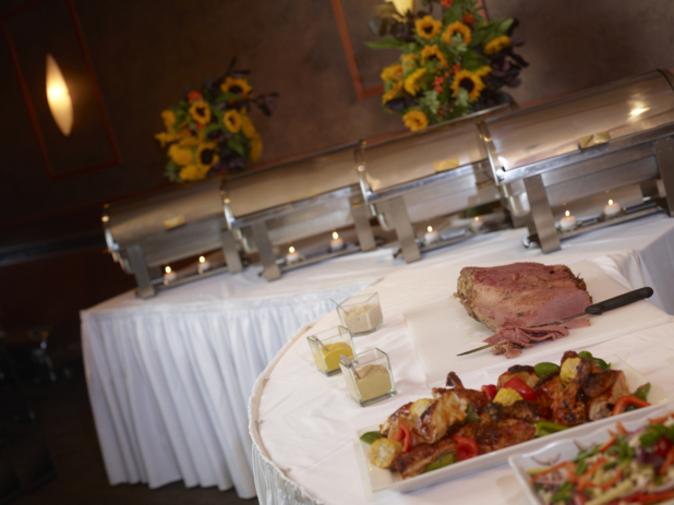 A white buffet table with a row of steamers and a corned beef, partially sliced, in foreground