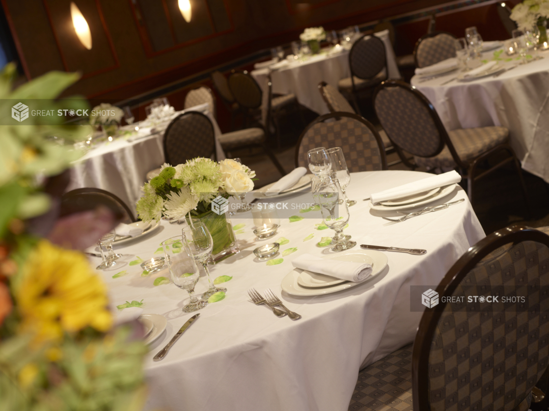 Dining tables adorned with white tablecloths and green and white flower arrangements at a catered event