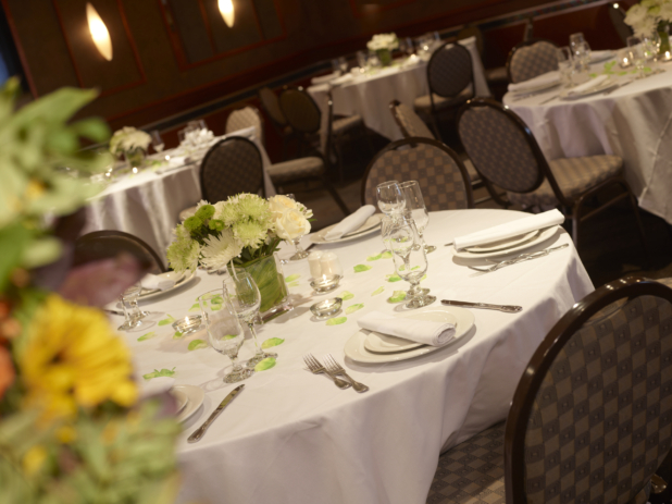 Dining tables adorned with white tablecloths and green and white flower arrangements at a catered event