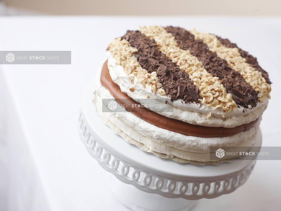 layered caramel crunch cake topped with chopped peanuts almonds and chocolate on a white cake stand