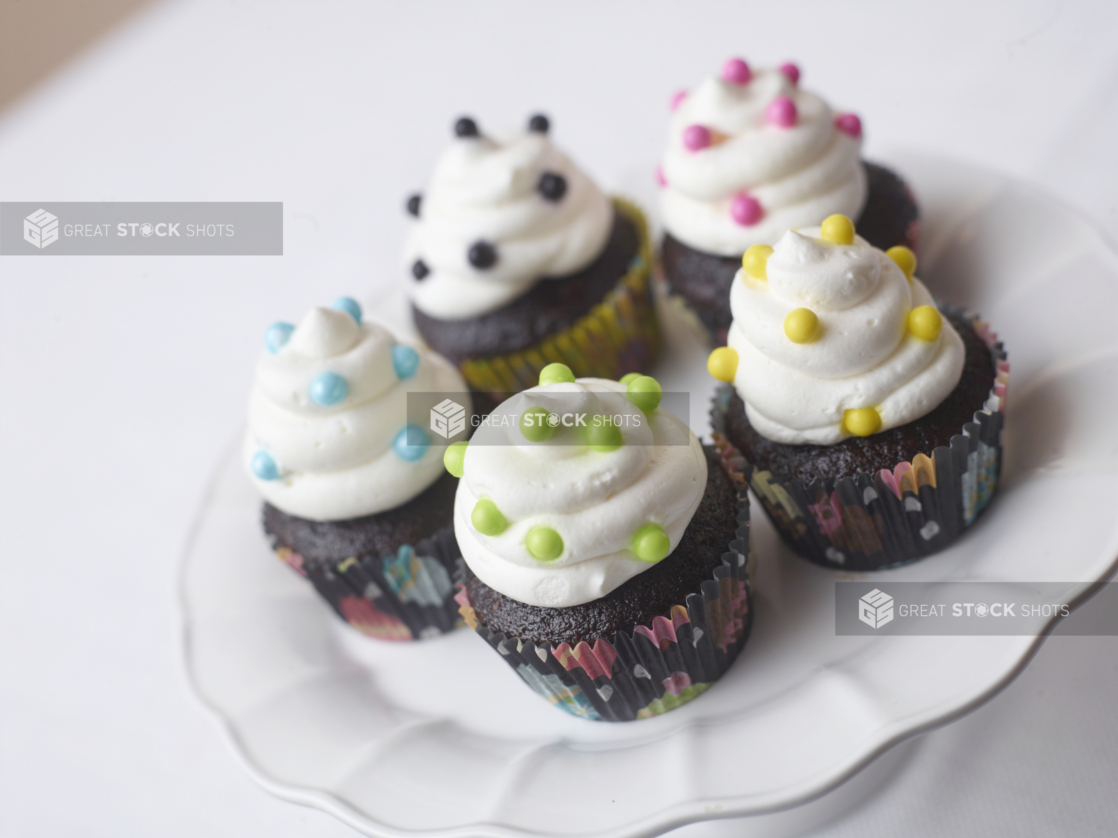 5 chocolate cupcakes with buttercream icing and colored candy pearls on a white cake stand