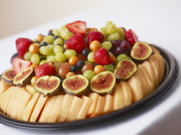 Honeydew fig strawberry blueberry green and red grape fruit tray on a white table cloth