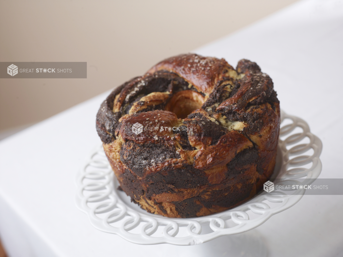 circular chocolate babka on a cake stand on white with a beige background,