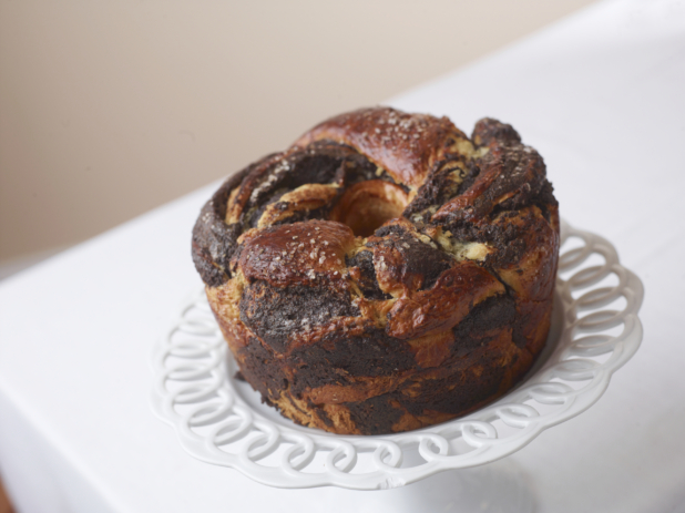 circular chocolate babka on a cake stand on white with a beige background,