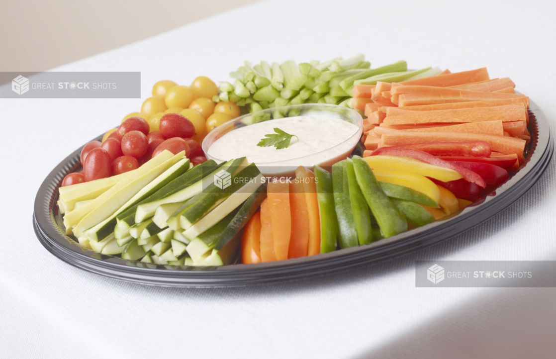 Round crudite veggie platter on black plastic tray white surface