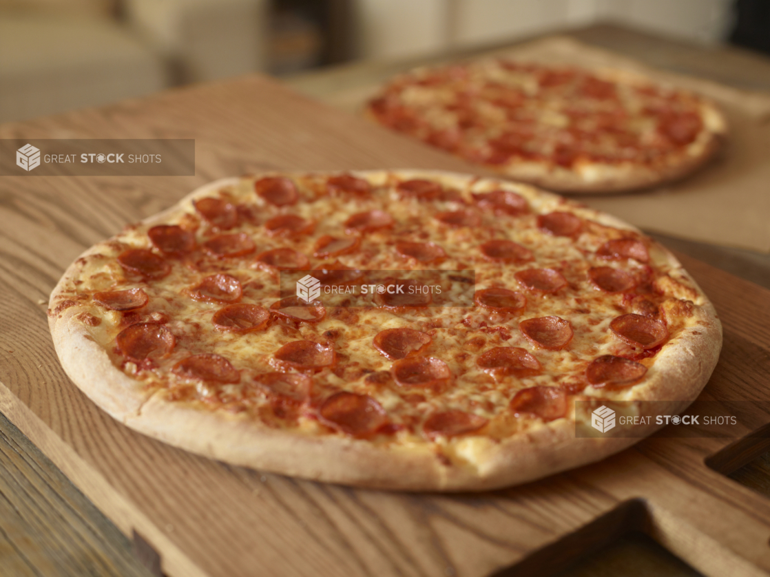 Whole, Uncut Pepperoni Pizzas on Wooden Cutting Boards on a Wooden Table