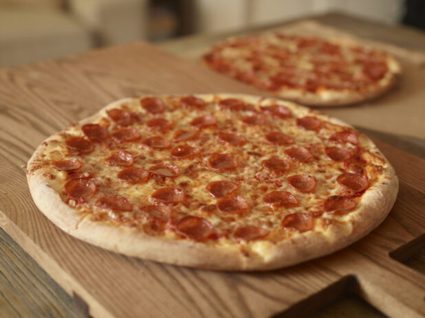 Whole, Uncut Pepperoni Pizzas on Wooden Cutting Boards on a Wooden Table