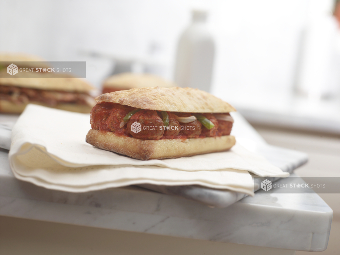 Meatball sandwich on a ciabatta bun on a napkin on a white marble countertop