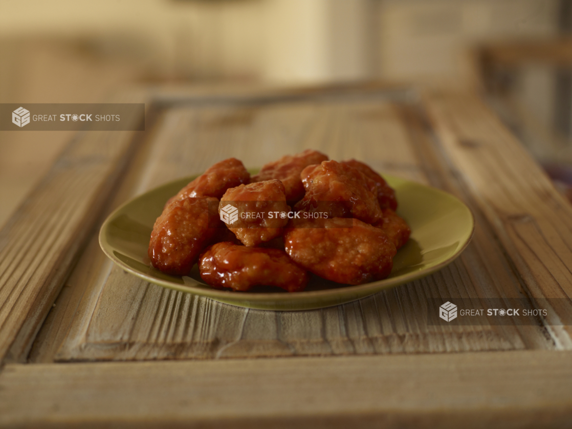 Sauced breaded chicken wings on a green plate on a rough wood surface