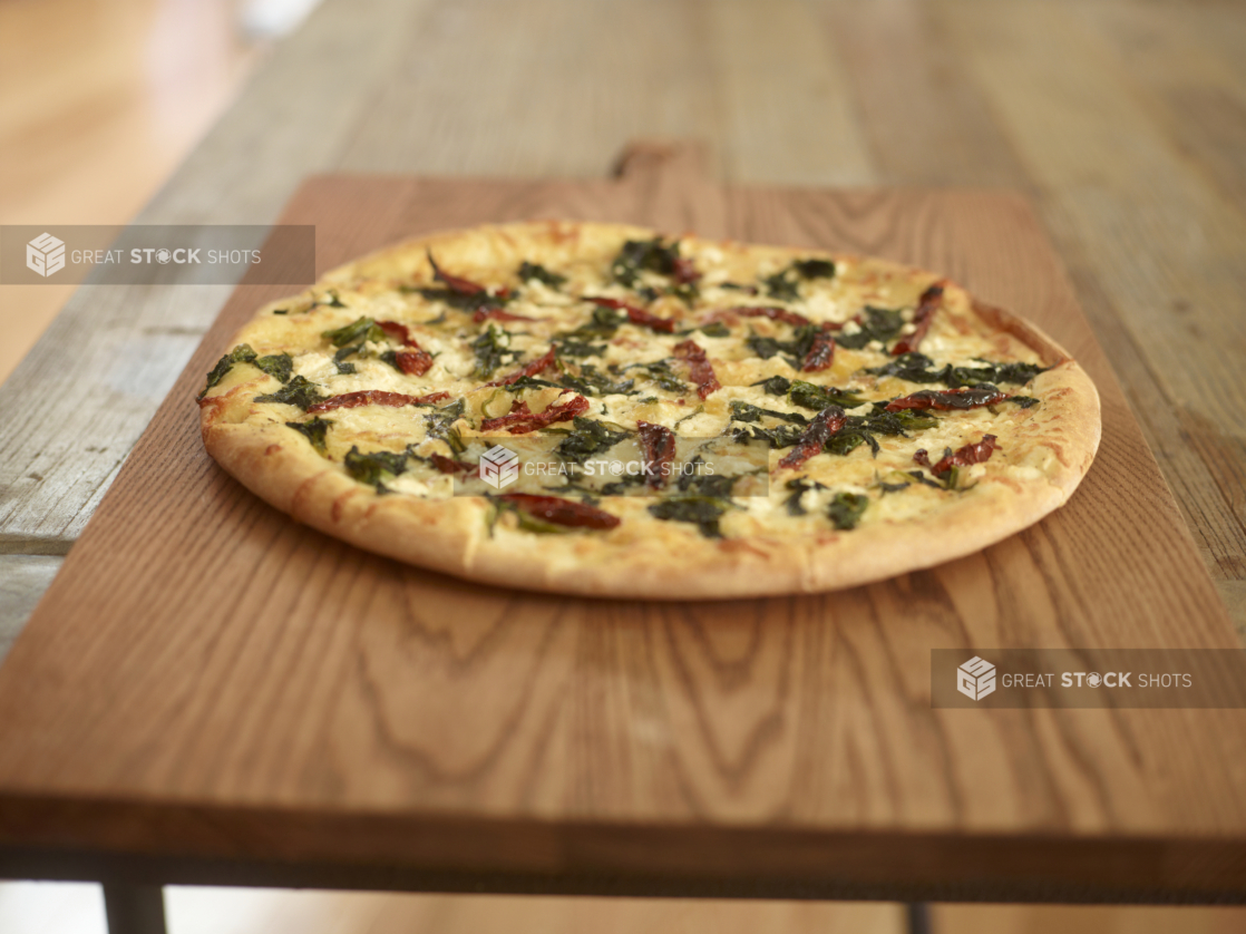 Whole pizza with goat cheese, roasted red peppers, and spinach on a wood board