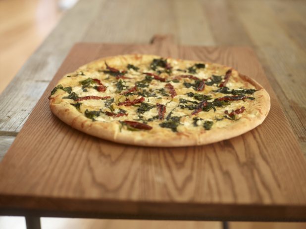 Whole pizza with goat cheese, roasted red peppers, and spinach on a wood board