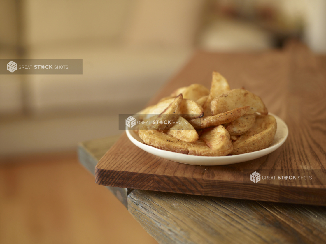 White plate of potato wedges on a wooden board on a wood tabletop