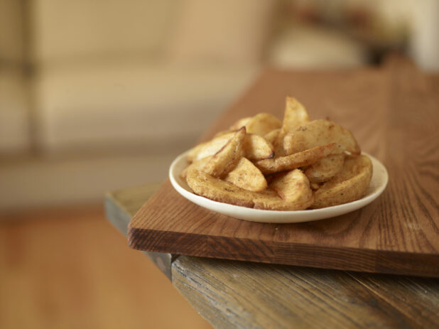 White plate of potato wedges on a wooden board on a wood tabletop