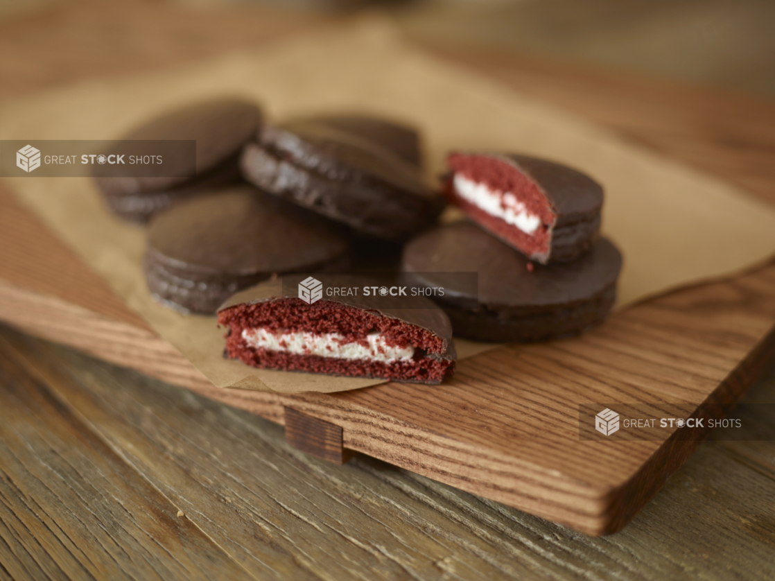 Chocolate snack cakes with white filling piled on parchment on a wood board