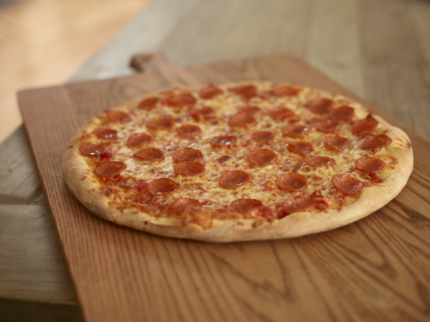 Whole unsliced pepperoni pizza on a wooden pizza peel