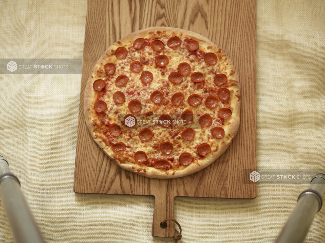 Whole pepperoni pizza on a wood board on a coarse cloth background