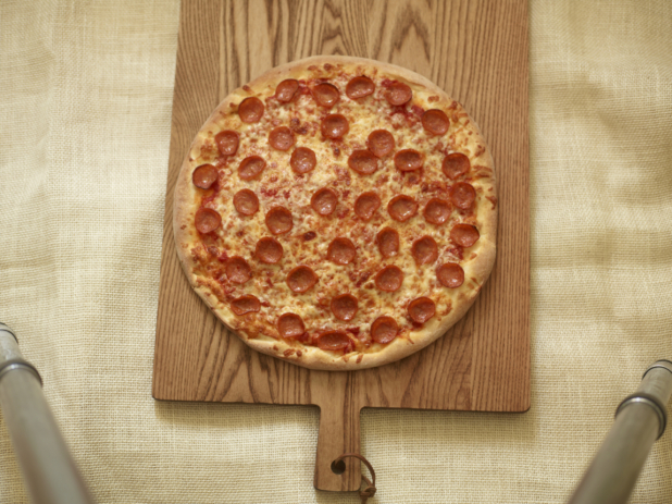 Whole pepperoni pizza on a wood board on a coarse cloth background