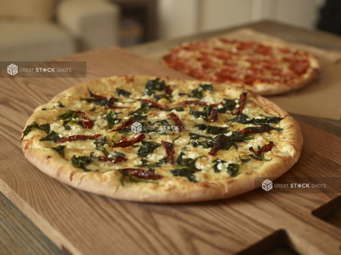 Whole, Uncut Spinach, Sun-dried Tomatoes and Feta Cheese Pizza and Pepperoni Pizza on Wooden Cutting Boards on a Wooden Table