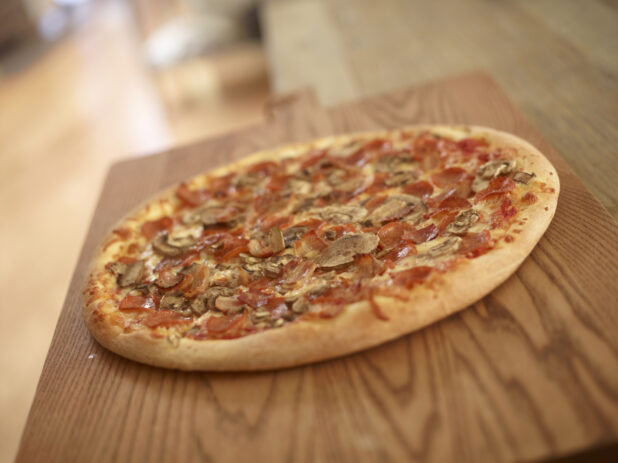 Whole Canadian Pizza with Pepperoni, Bacon and Mushrooms on a Wooden Cutting Board in a Dining Room Setting