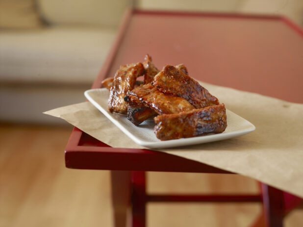 Sauced barbecue ribs on a white plate on a red table, close-up