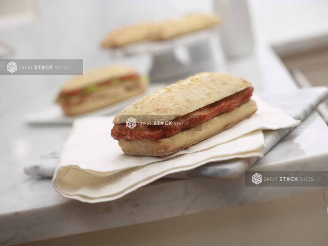 Veal or Chicken Cutlet Sandwich with Marinara Sauce on a Ciabatta Bun on a White Cloth and Marble Surface in an Indoor Setting