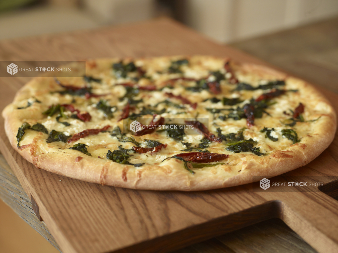 Whole, Uncut Spinach, Sun-dried Tomatoes and Feta Cheese Pizza on Wooden Cutting Boards on a Wooden Table