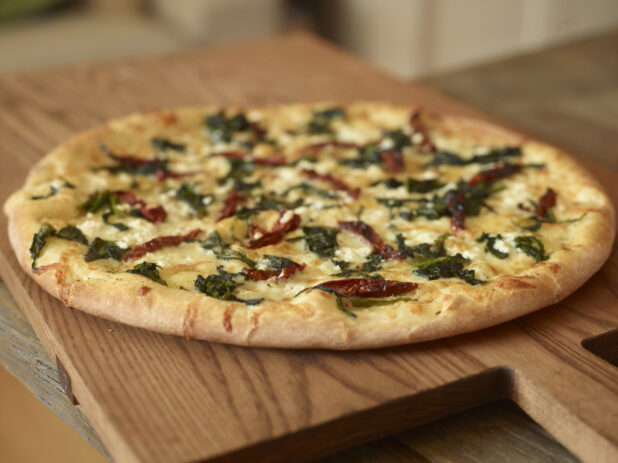 Whole, Uncut Spinach, Sun-dried Tomatoes and Feta Cheese Pizza on Wooden Cutting Boards on a Wooden Table