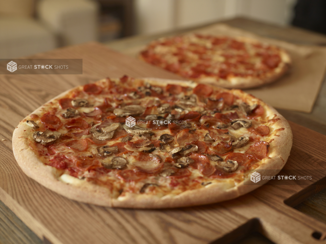 Whole, Uncut Meat Lovers Pizza and Pepperoni Pizza on Wooden Cutting Boards on a Wooden Table