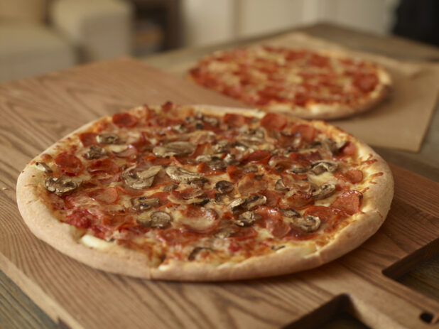 Whole, Uncut Meat Lovers Pizza and Pepperoni Pizza on Wooden Cutting Boards on a Wooden Table