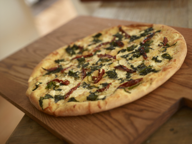 Whole 3-Topping Pizza with Sautéed Spinach, Sun-dried Tomatoes and Feta Cheese on a Wooden Cutting Board in a Dining Room Setting
