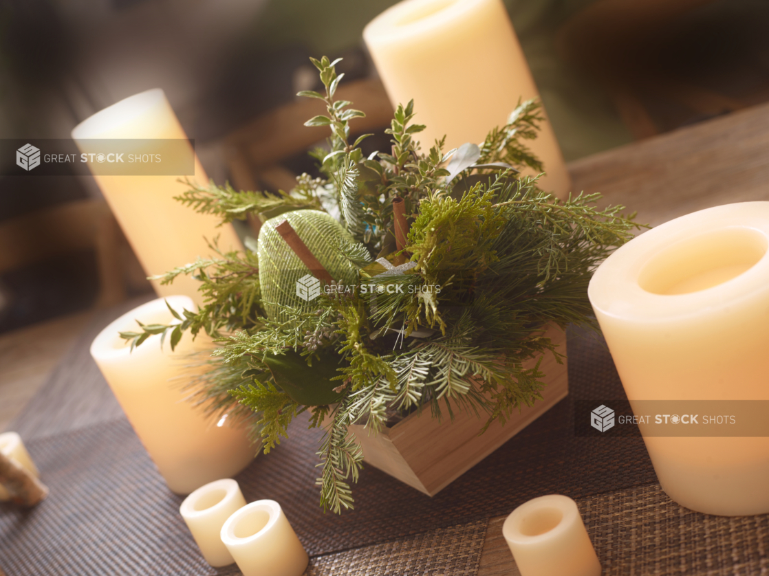 Table decorated for Christmas with greenery arrangement in a wood catering tray surrounded by white candles