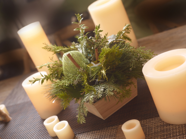 Table decorated for Christmas with greenery arrangement in a wood catering tray surrounded by white candles
