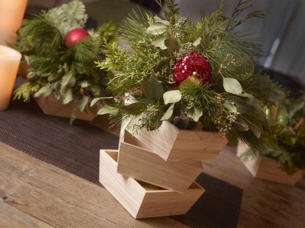 Table decorated for Christmas with greenery arrangements in wood catering trays and candles