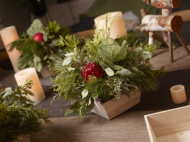 Table decorated for Christmas with greenery arrangements in wood catering trays, candles, and folk art