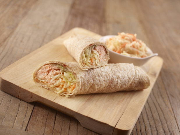 Salmon and Shredded Vegetables in a Whole Wheat Wrap Cut in Half on a Wooden Cutting Board with a Side Dish of Coleslaw on a Rustic Wooden Surface