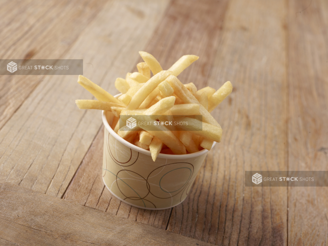 Thick Cut Plain French Fries in a Paper Take-Out Bowl on a Weathered Wooden Surface in an Indoor Setting