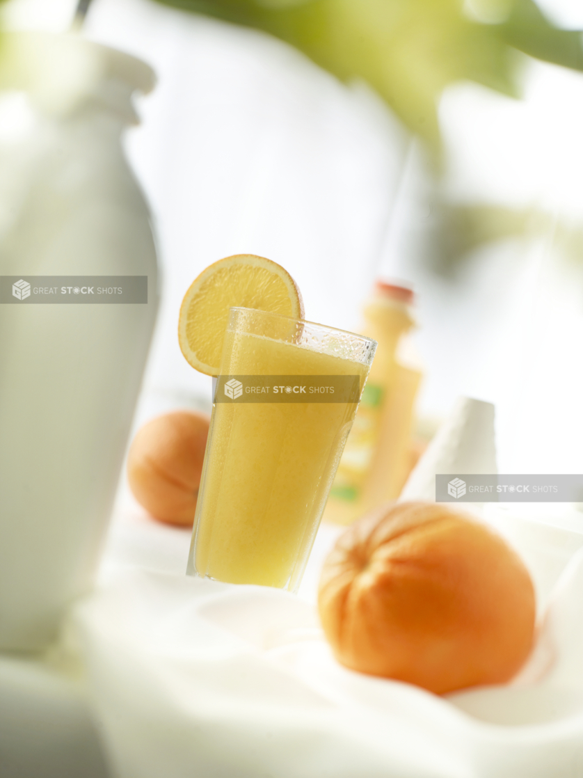 A glass of freshly-squeezed orange juice with fresh oranges on white, bokeh