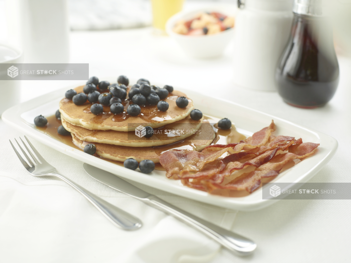 A Platter of Pancakes and Blueberries with a Side of Bacon on a White Table Cloth in a Restaurant Setting