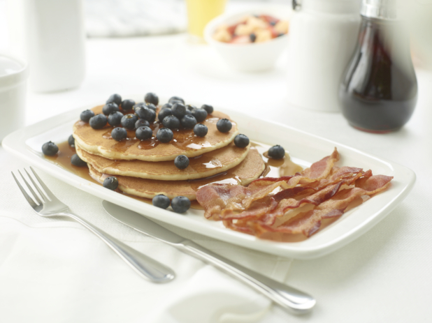 A Platter of Pancakes and Blueberries with a Side of Bacon on a White Table Cloth in a Restaurant Setting