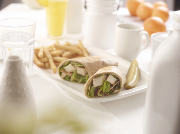 Salad wrap sandwich with chicken in two pieces on a plate with a pickle and french fries, white table setting