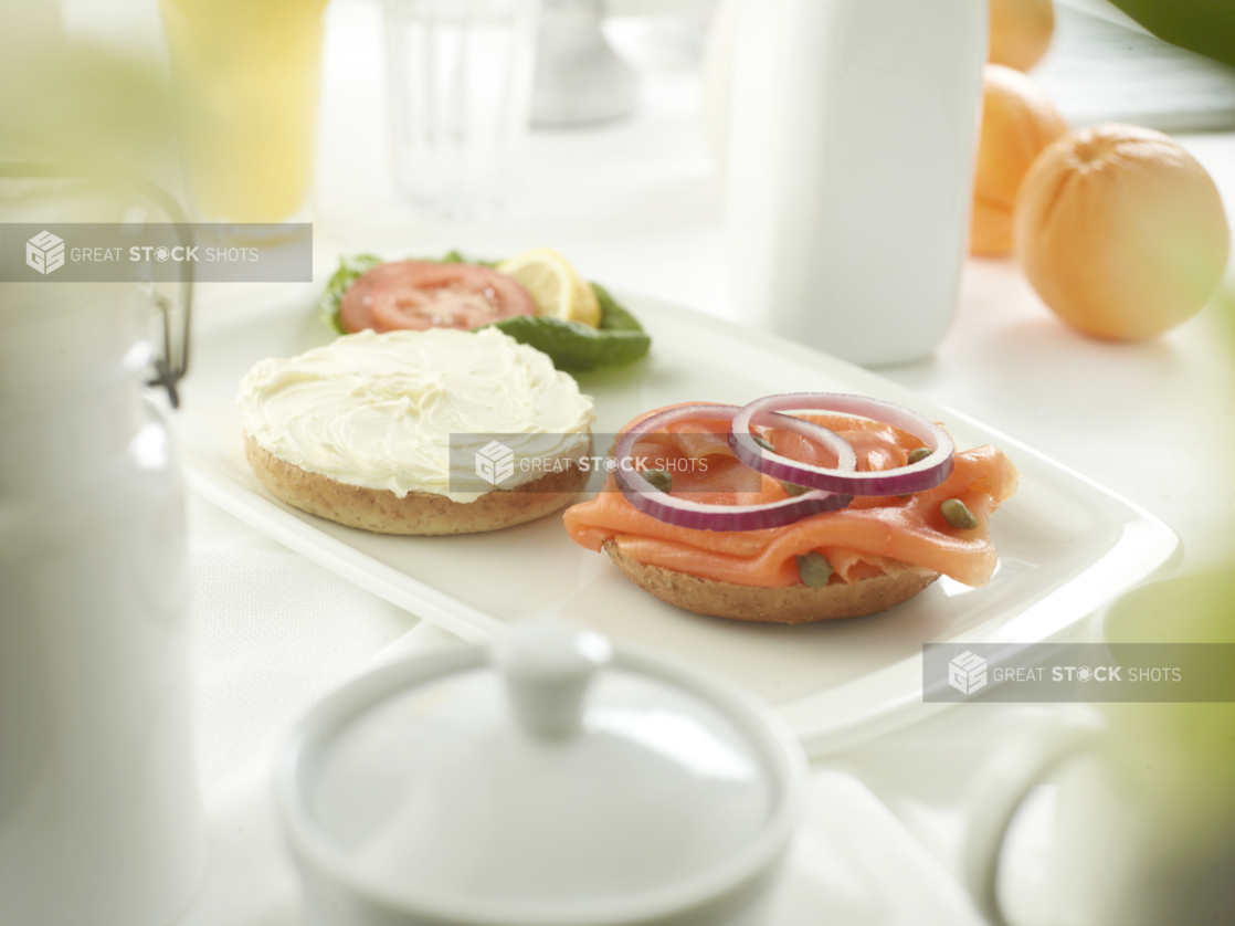 A bagel cream cheese on one half, and lox with capers and sliced red onion on the other, white table setting