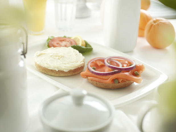 A bagel cream cheese on one half, and lox with capers and sliced red onion on the other, white table setting