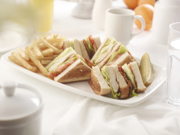 Chicken club sandwich, quartered, with french fries, on a square white plate in an all-white table setting