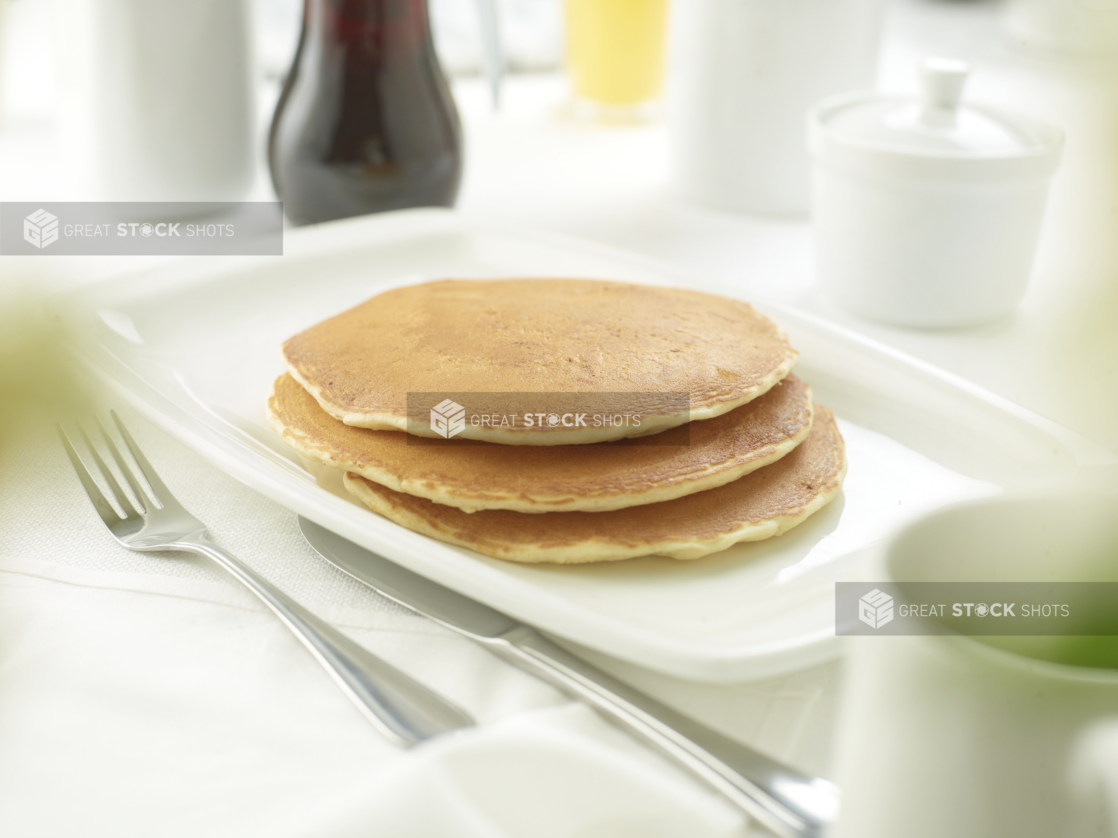 A Stack of Plain Pancakes on a White Ceramic Platter on a White Table Cloth Surface in a Restaurant Setting