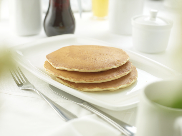 A Stack of Plain Pancakes on a White Ceramic Platter on a White Table Cloth Surface in a Restaurant Setting