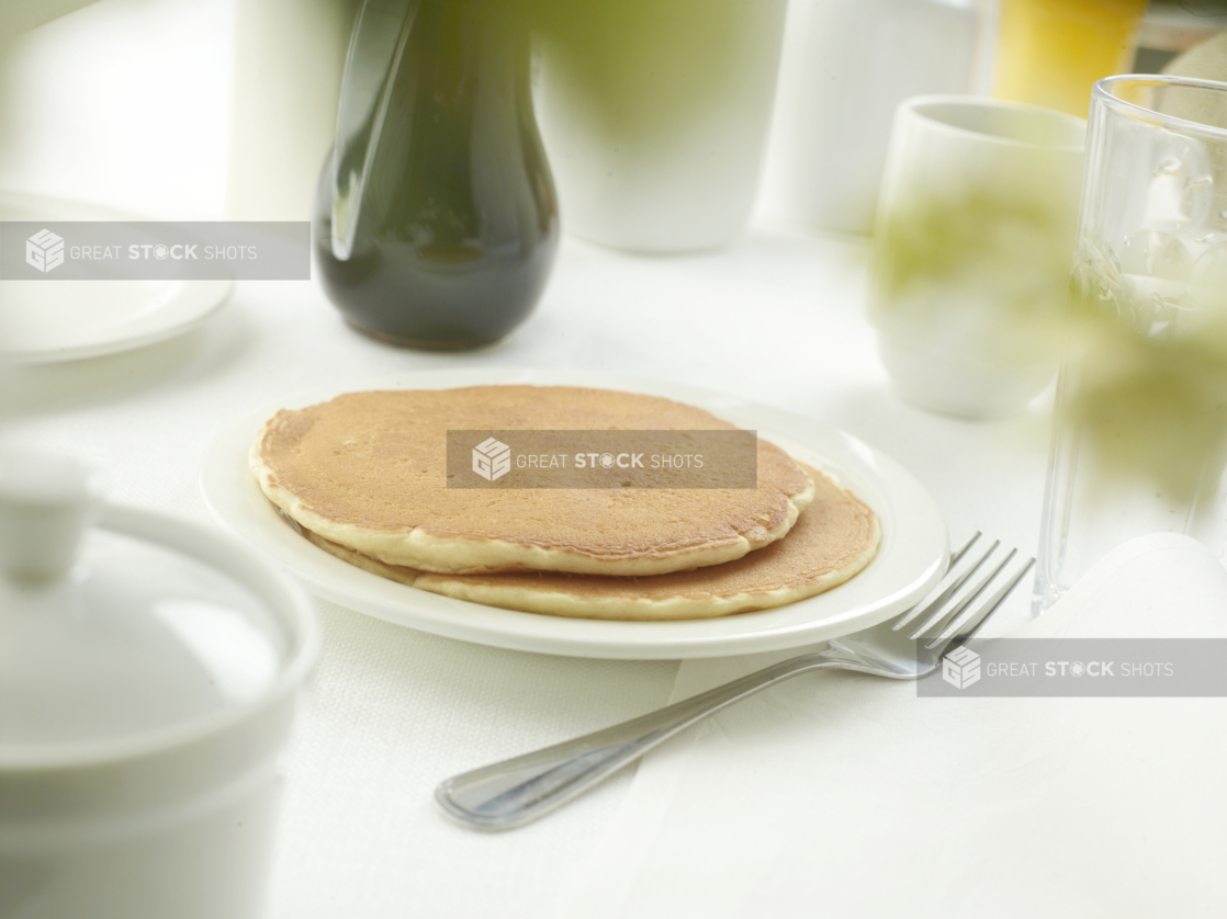 A Couple of Plain Pancakes on a White Ceramic Dish on a White Table Cloth Surface in a Restaurant Setting