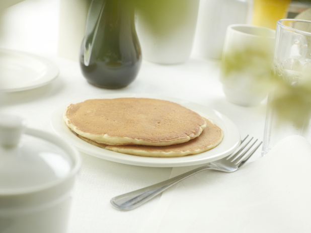 A Couple of Plain Pancakes on a White Ceramic Dish on a White Table Cloth Surface in a Restaurant Setting