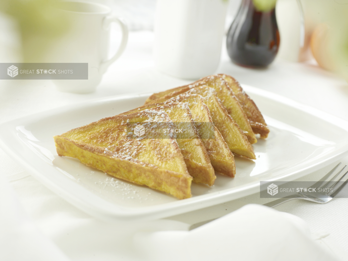 French toast on a square white plate in an all-white table setting