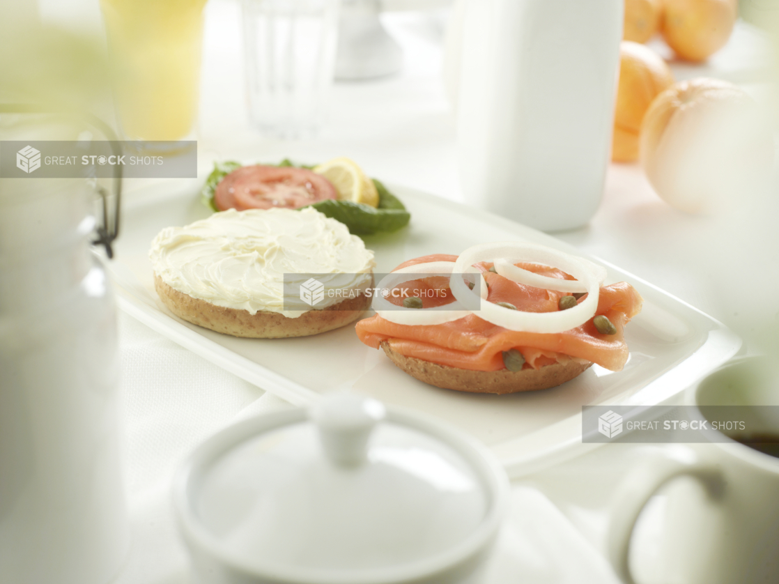 A bagel cream cheese on one half, and lox with capers and sliced white onion on the other, white table setting