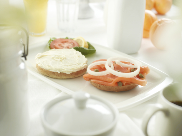 A bagel cream cheese on one half, and lox with capers and sliced white onion on the other, white table setting
